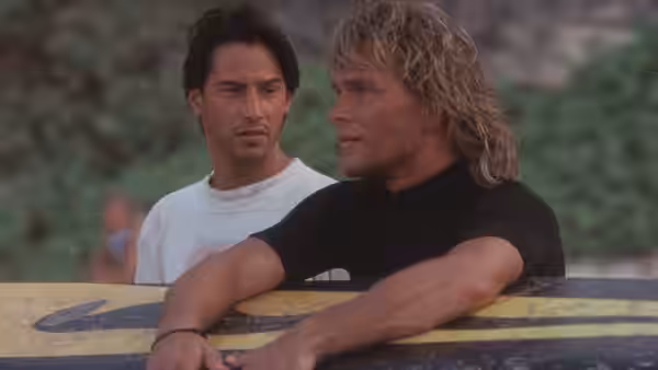 Johnny Utah (Keanu Reeves) and Bodhi (Patrick Swayze) leaning on a surfboard