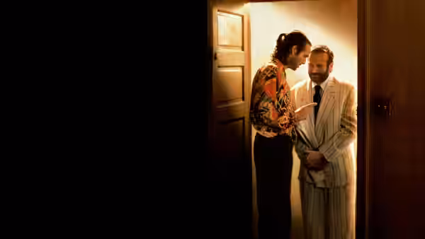 Two men stand close together talking in a dimly lit doorway