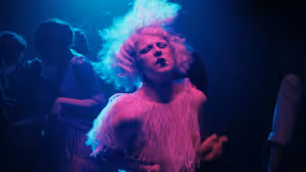Woman with bright pink hair dances in a crowded nightclub under blue lights