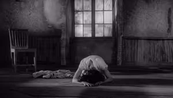 A woman bends over with her head resting on the floor in a bare room