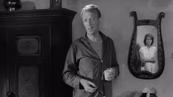 David (Gunnar Björnstrand) holds a cup beside Karin’s reflection in a wall mirror