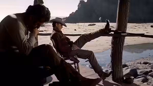 A man leans forward beside another man reclining in a chair by the shore