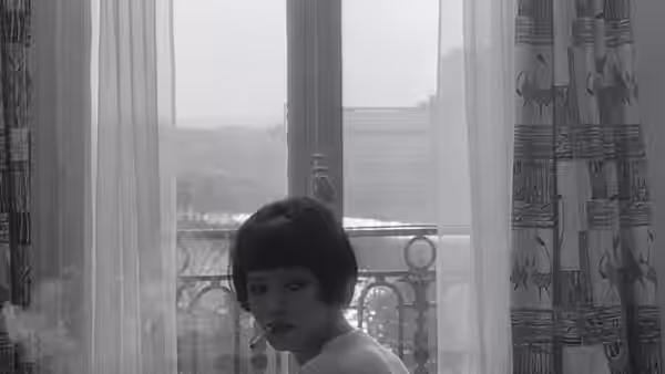 Nana Kleinfrankenheim (Anna Karina) smokes beside a tall window