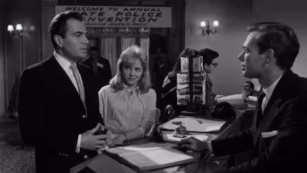 Humbert Humbert (James Mason) and Lolita (Sue Lyon) stand at a hotel reception desk