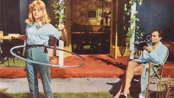 Lolita (Sue Lyon) stands with a hula hoop while Humbert Humbert (James Mason) reads nearby
