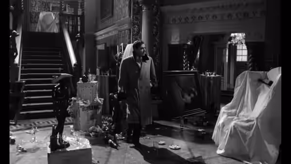 Humbert Humbert (James Mason) stands among covered furniture in a cluttered room