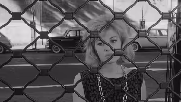 Vittoria (Monica Vitti) looks through a metal lattice as a car passes behind her