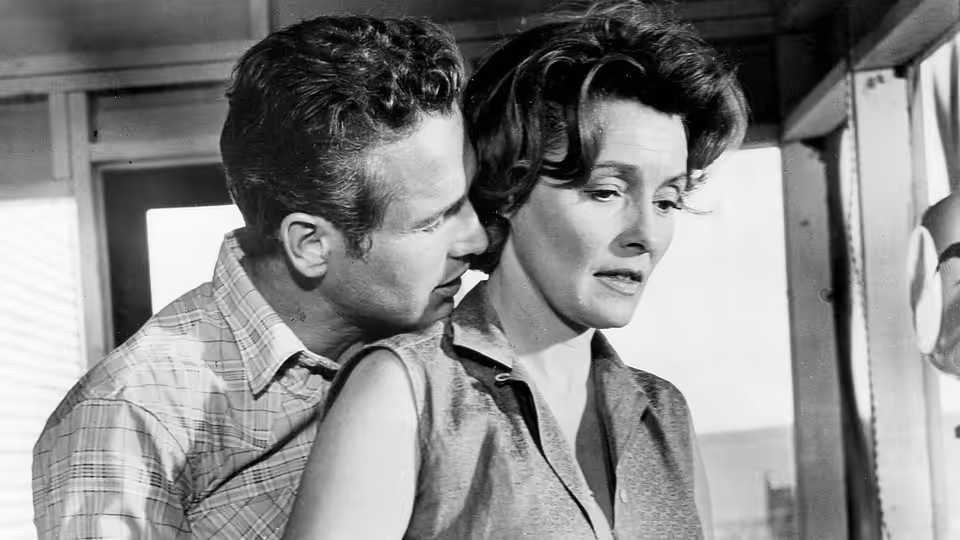 Hud Bannon (Paul Newman) leans close to Alma Brown (Patricia Neal) indoors