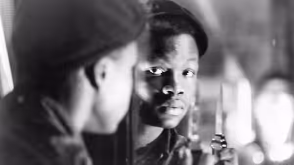 A young man in a beret looks past someone standing close in the foreground