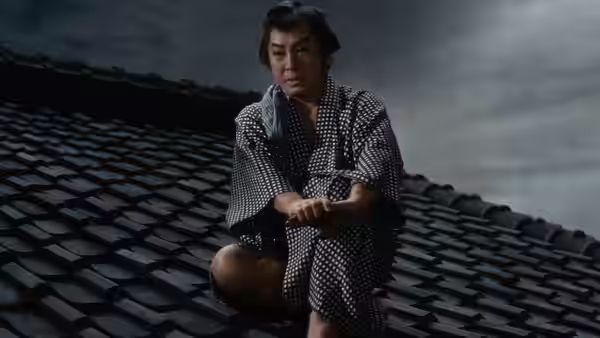 Yukinojo Nakamura (Kazuo Hasegawa) kneels on a tiled rooftop in patterned robes