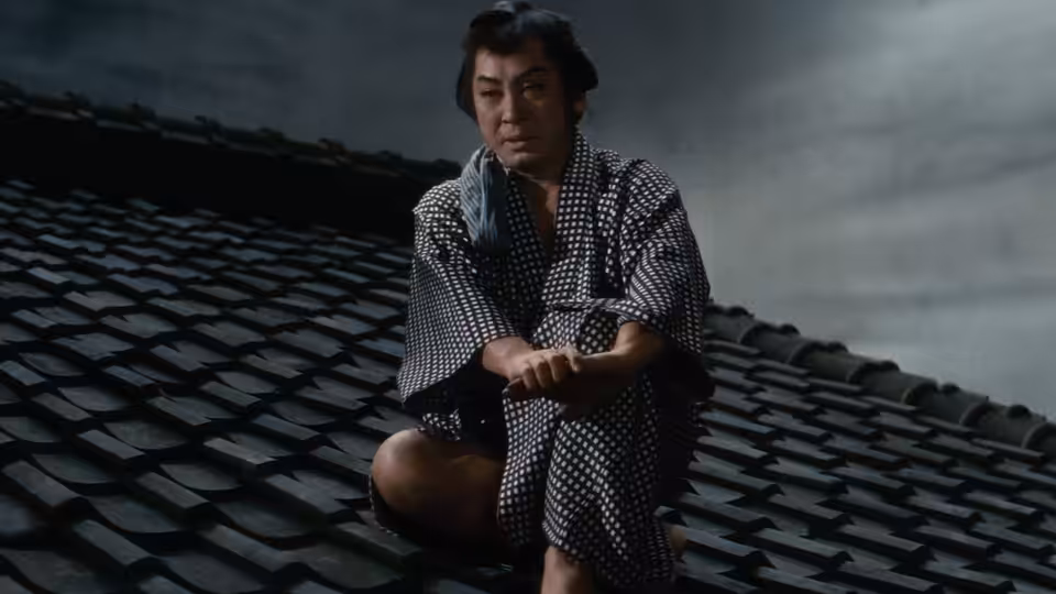 Yukinojo Nakamura (Kazuo Hasegawa) kneels on a tiled rooftop in patterned robes