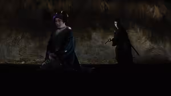 Two robed figures face each other in a dim cave, one holding a staff