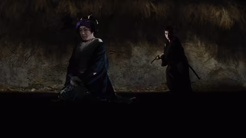 Two robed figures face each other in a dim cave, one holding a staff