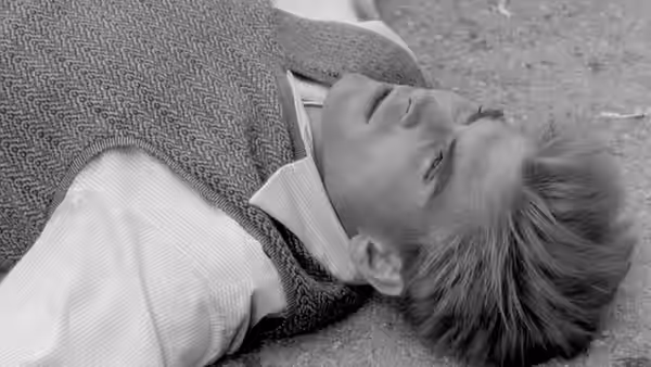 A young man lies on the ground, his head turned to one side