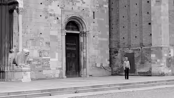 A man stands alone across a broad square before an ornate stone building