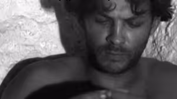 A young man lies with his eyes closed, his face turned toward the light