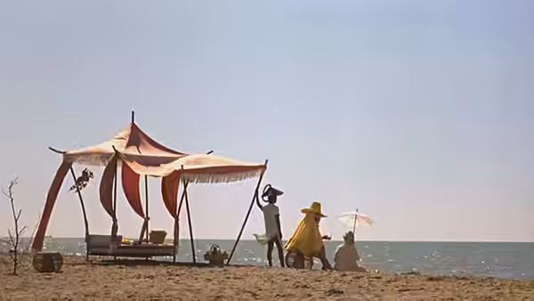 A small group gathers beside a striped beach canopy on the shore