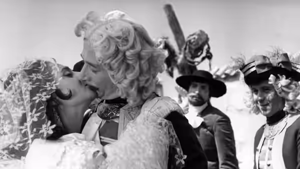 A woman kisses a blonde woman while two men in broad hats look on