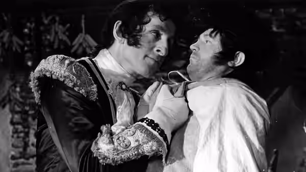 A uniformed man grips another man by the collar in a dim room
