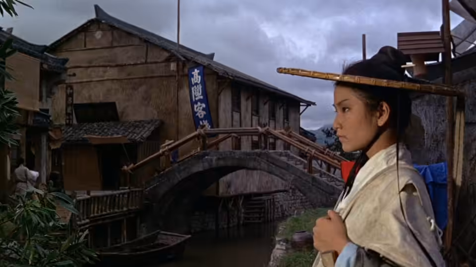 Golden Sparrow (Cheng Pei-pei) stands beside a wooden bridge in a riverside town