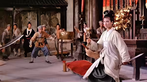 Golden Sparrow (Cheng Pei-pei) kneels with a sword while martial artists spar behind her