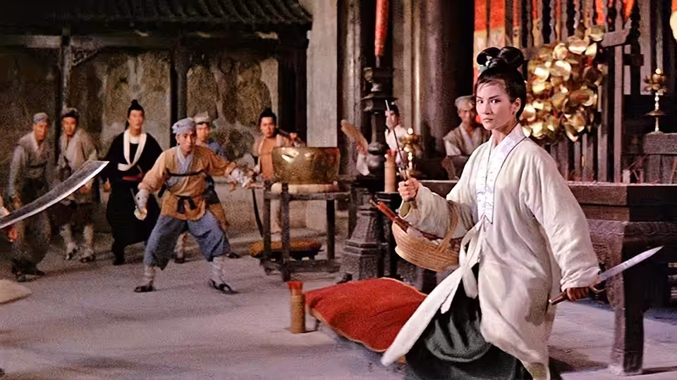 Golden Sparrow (Cheng Pei-pei) kneels with a sword while martial artists spar behind her