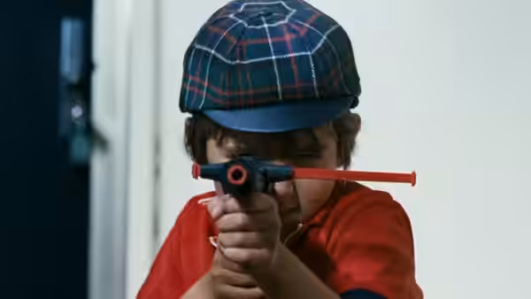 A child in a plaid cap aims a toy gun forward