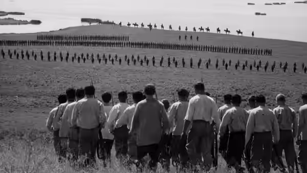 A group of men walk toward lines of soldiers along the shoreline