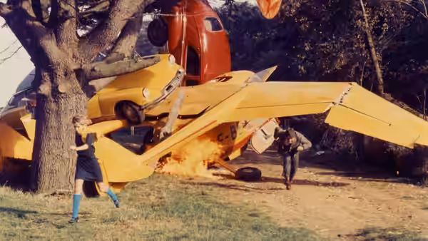 Corinne and another woman stand beside a yellow airplane on a country road