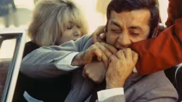 Corinne clings to Roland as he bites the sleeve of a red-clad person