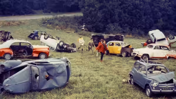 Corinne and Roland walk among overturned and abandoned cars in a field