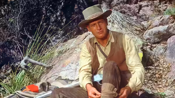 John Russell (Paul Newman) sits among rocks, adjusting his boot
