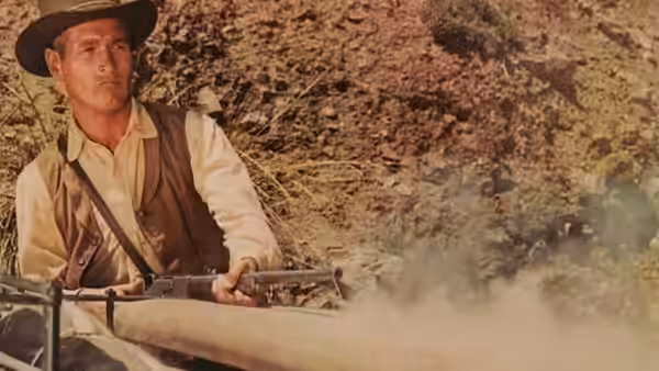 John Russell (Paul Newman) holds a rifle as a wagon moves through dust