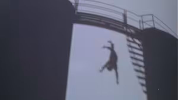 A figure falls from an elevated structure against the pale sky