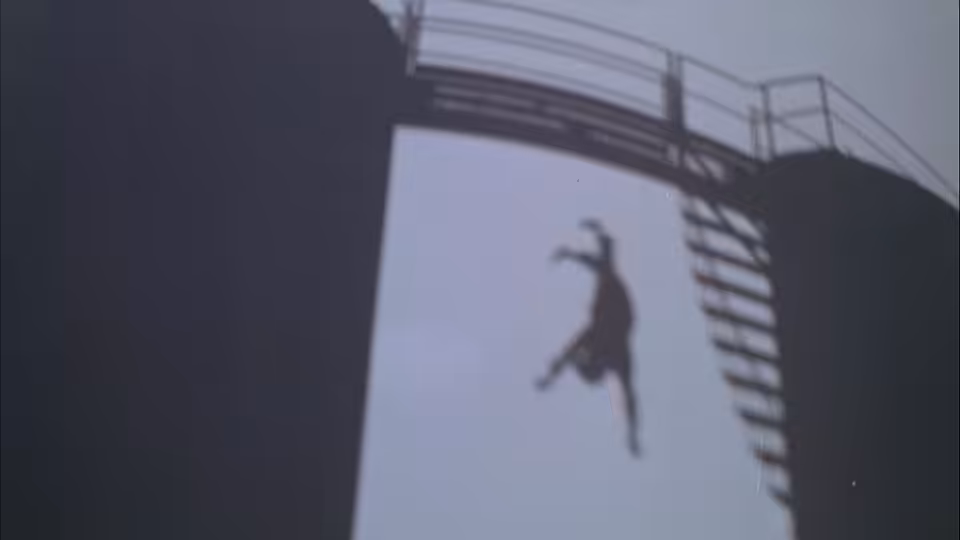 A figure falls from an elevated structure against the pale sky