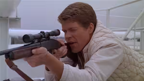 Bobby Thompson (Tim O'Kelly) peers through a rifle scope on a rooftop