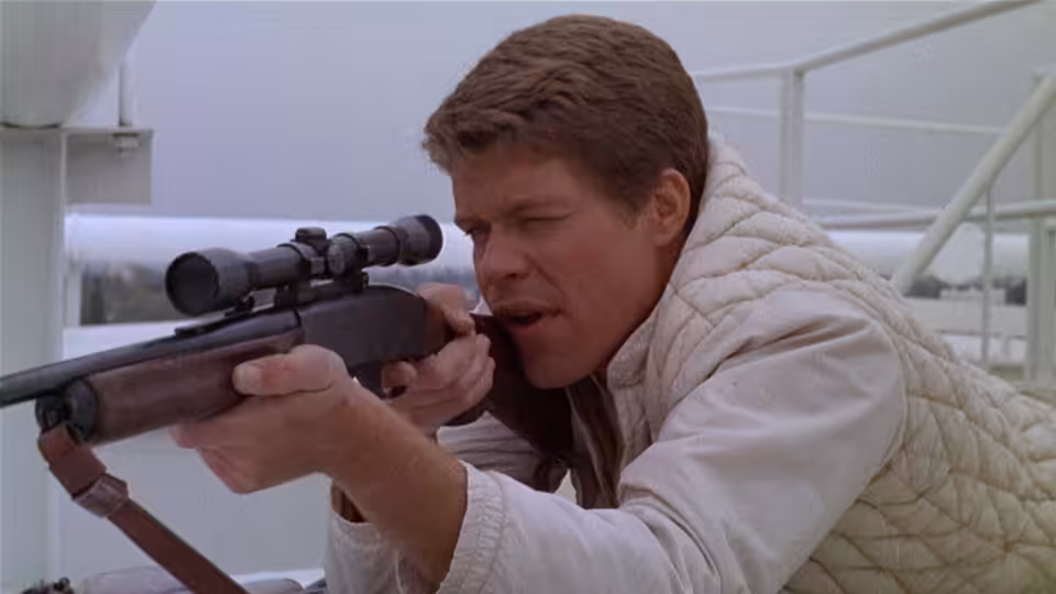 Bobby Thompson (Tim O'Kelly) peers through a rifle scope on a rooftop