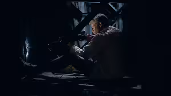 Bobby Thompson (Tim O'Kelly) aims a rifle from a darkened structure