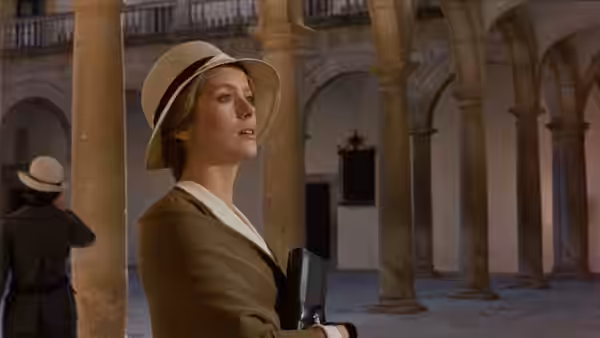 Tristana (Catherine Deneuve) in a wide-brimmed hat stands beneath a columned arcade