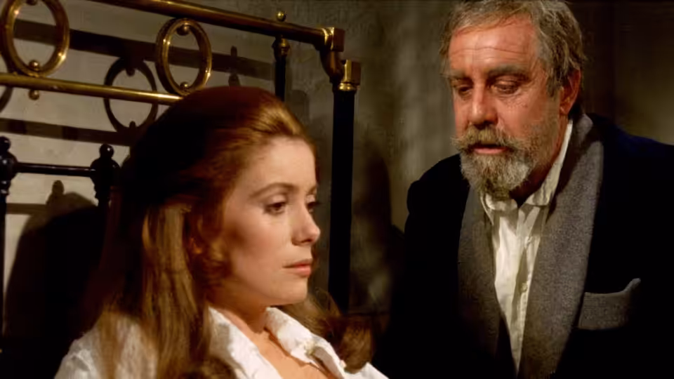 Tristana (Catherine Deneuve) and Don Lope (Fernando Rey) stand beside a coat rack