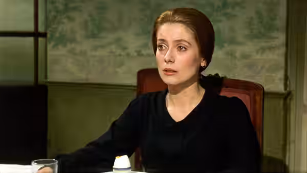 Tristana (Catherine Deneuve) sits at a table in a furnished room