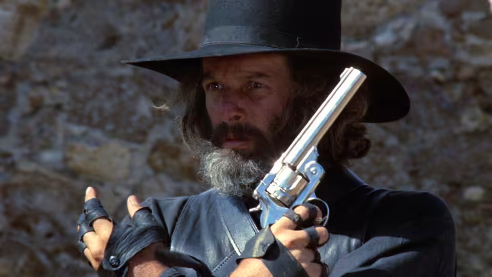 El Topo (Alejandro Jodorowsky) holds a revolver before a stone wall