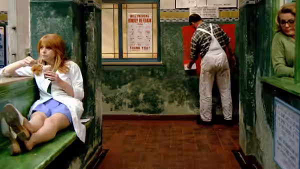 Susan sits on a bench holding a cup while a man stands at a service window