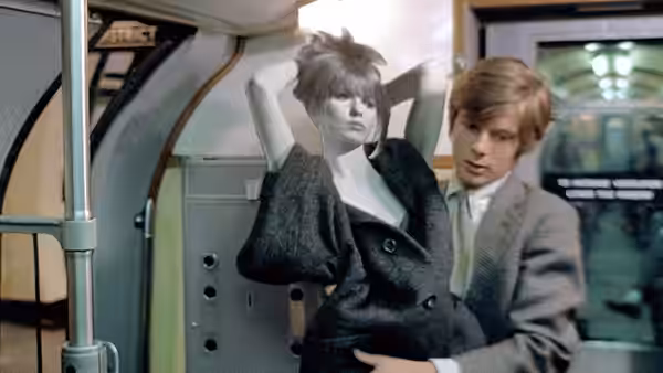 Mike (John Moulder-Brown) supports a woman in a dark coat inside a train