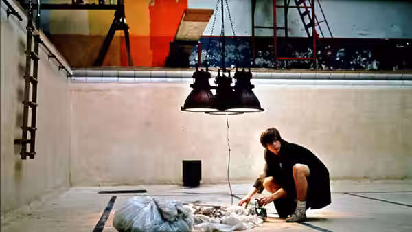A young man kneels beside a person lying beneath a hanging lamp in an indoor pool
