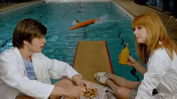 Mike and Susan sit opposite each other beside the swimming pool, handling a small object