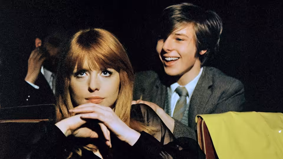 Susan (Jane Asher) sits at a table as Mike (John Moulder-Brown) smiles beside her