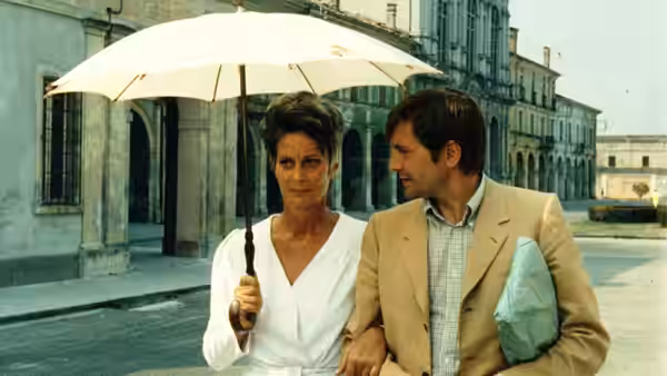 Draifa (Alida Valli) walks beneath an umbrella beside Athos Magnani Jr. (Giulio Brogi) outside a building