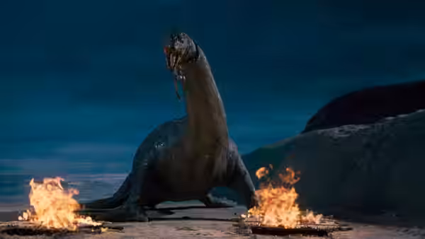 A long-necked dinosaur stands beside flames on a rocky shore