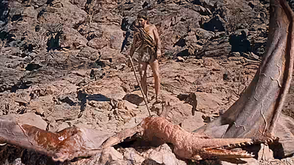 A man holding a spear stands beside the enormous limb of a dinosaur